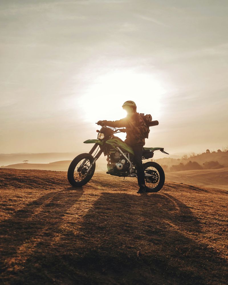 A rider on a petrol off-road motorcycle silhouetted on a hilltop at sunset